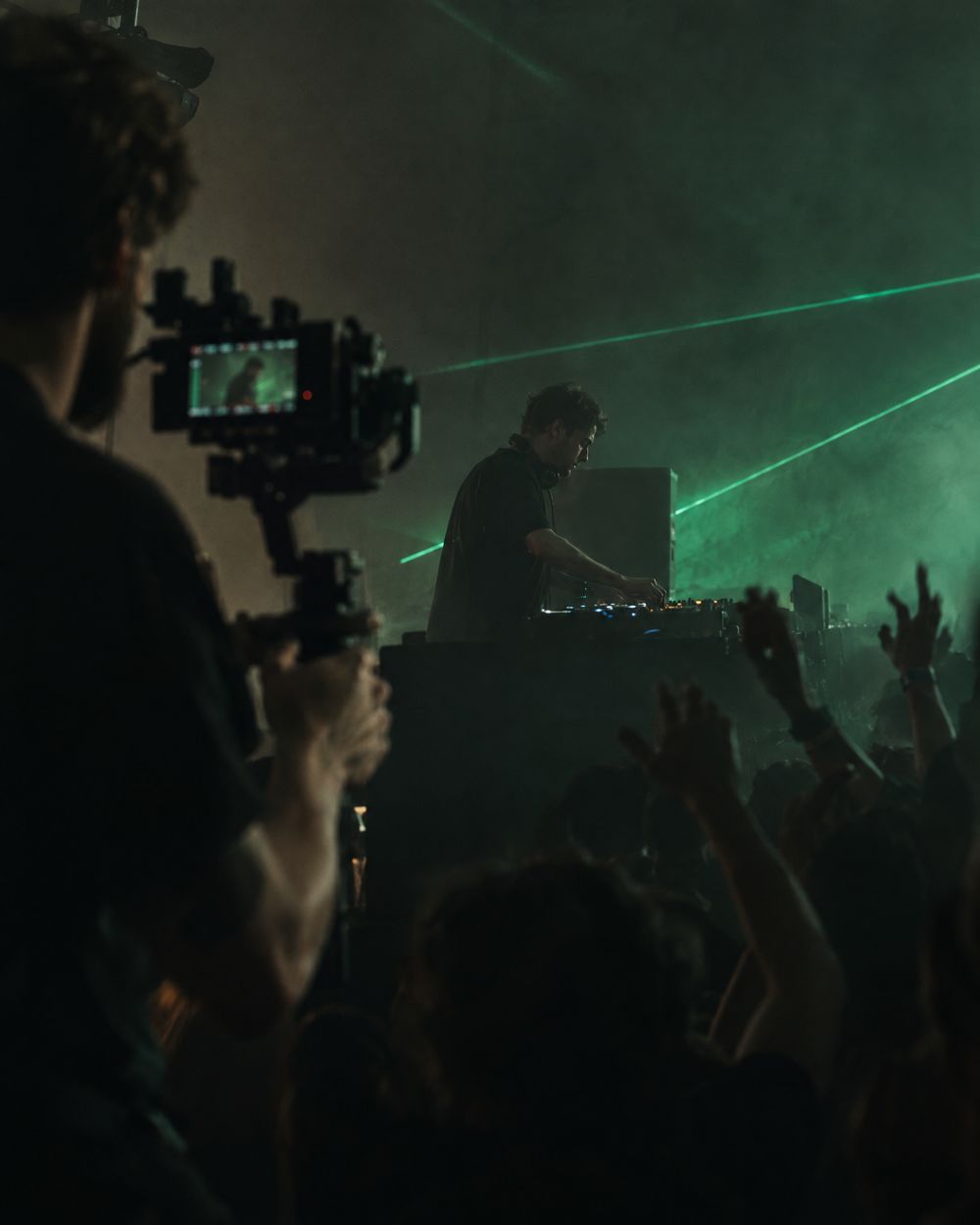 A DJ at the decks in a club, the crowd and the green lasers